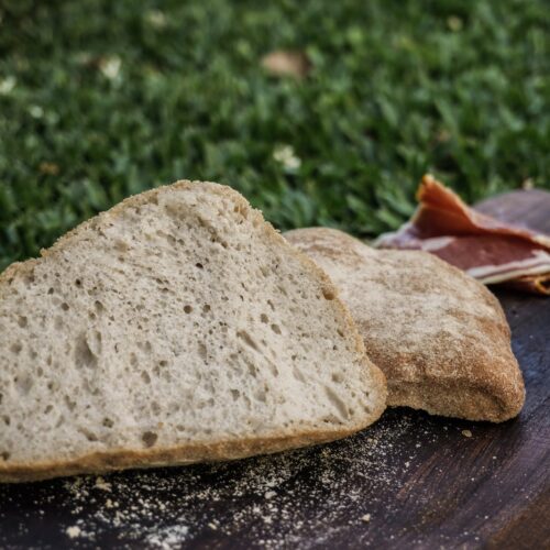 Ciabatta sin gluten cortada mostrando su miga, sobre una tabla en el pasto