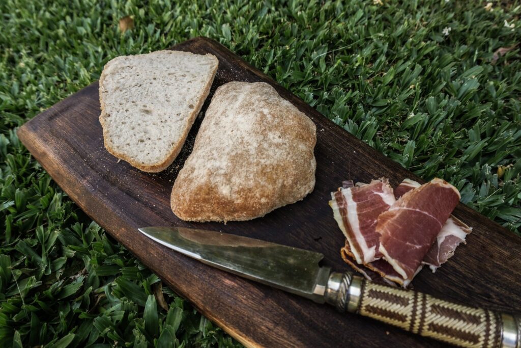Ciabatta sin gluten entera y cortada sobre una tabla con jamón crudo y cuchillo