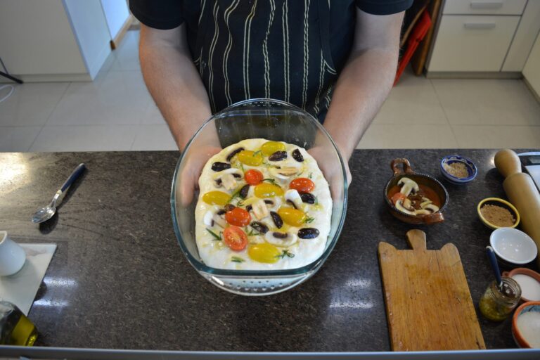 Focaccia sin gluten cubierta con tomates cherry, champiñones, aceitunas y romero, lista para el horno