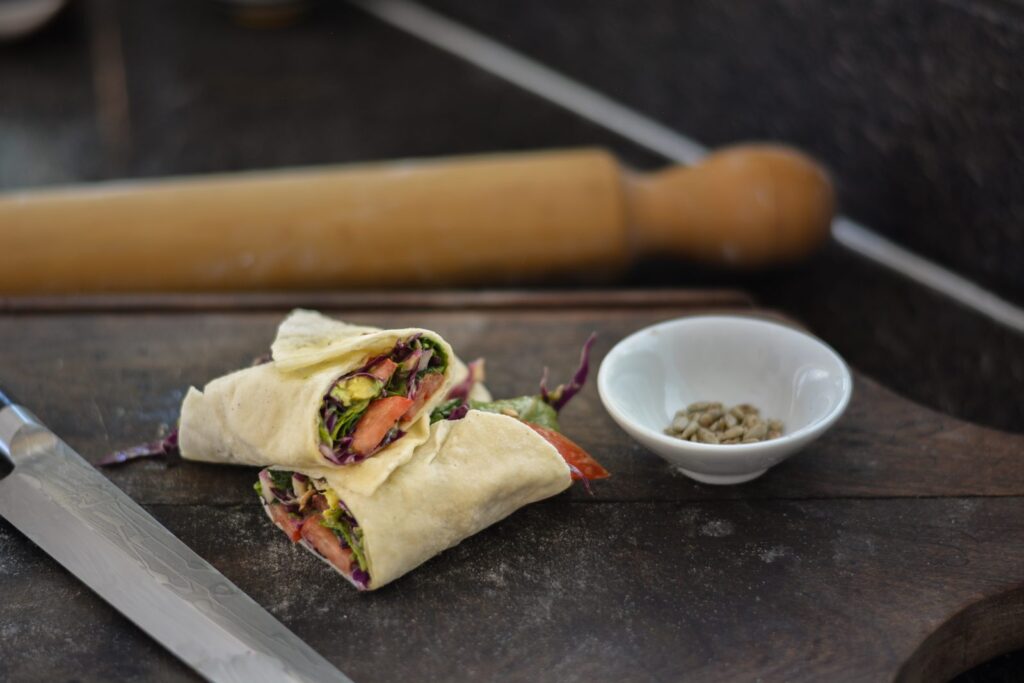 Rapiditas sin gluten veganas rellenas con palta, repollo morado, tomate y rúcula, cortadas al medio sobre una tabla de madera