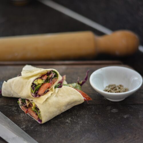 Rapiditas sin gluten veganas rellenas con palta, repollo morado, tomate y rúcula, cortadas al medio sobre una tabla de madera