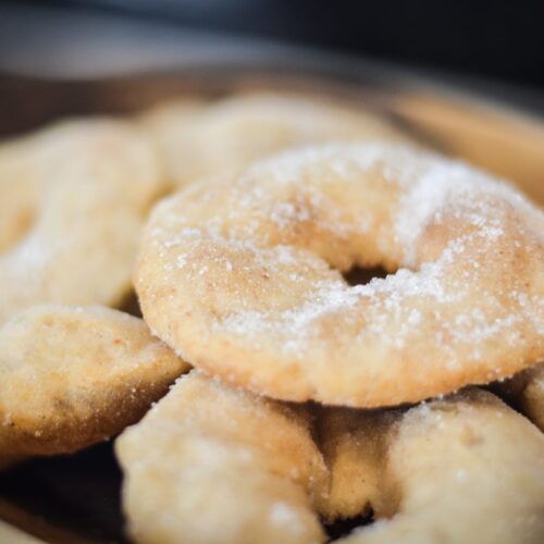 Tortas fritas sin gluten espolvoreadas con azúcar, apiladas en una fuente de madera